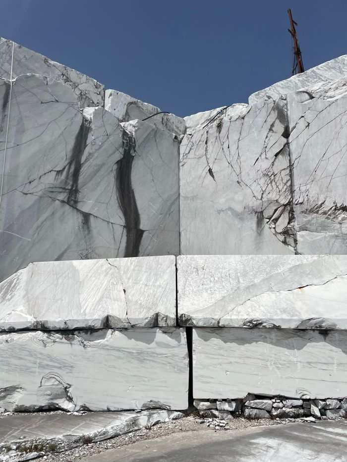Large white marble blocks with cracks in an open quarry under clear blue sky.
